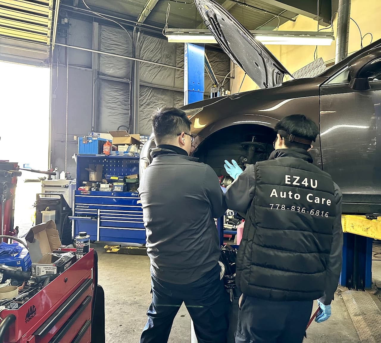 Two EZ4U Auto Care technicians in branded jackets working on the front wheel of a car raised on the hoist in the Richmond shop